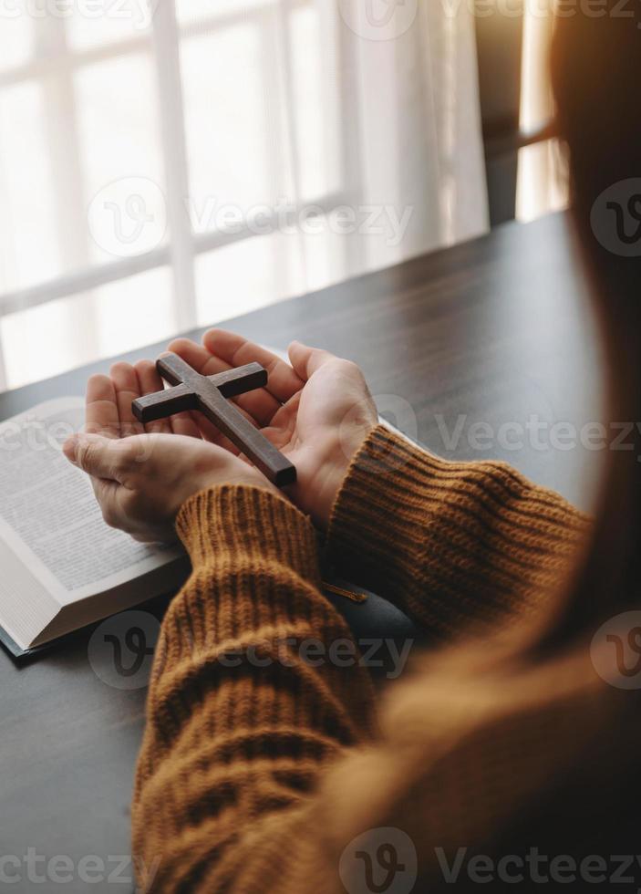 frau, die sitzt und die schriften studiert. das holzkreuz in den händen. christliche bildungskonzepte die heilige schrift öffnen und beten foto