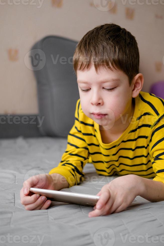 Ein Teenager liegt mit einem Telefon in den Händen auf der Couch. Das Kind spielt zu Hause im Telefon. Erholung mit dem Telefon. Urlaub mit Gadgets. foto