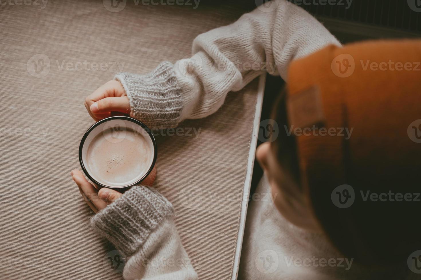 hände in einem pullover halten heißen kakao in einem roten becher, draufsicht. ein gemütliches foto mit einem becher in der hand mit kopierraum. Kind trinkt heiße Schokolade