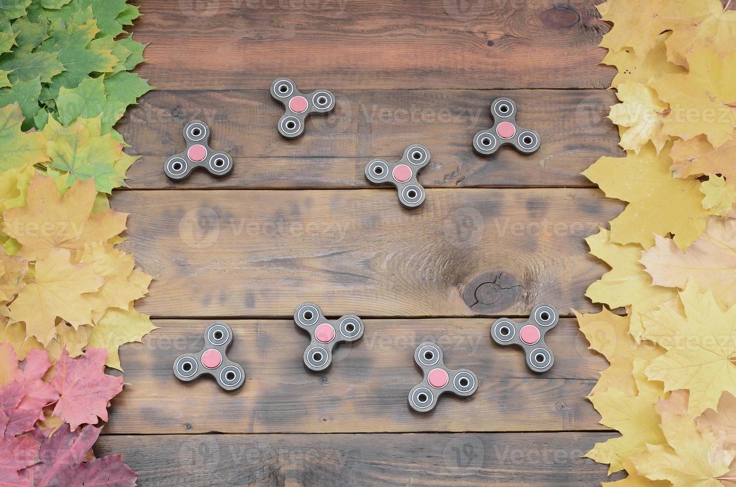 Mehrere Spinner unter den vielen vergilbten gefallenen Herbstblättern auf der Hintergrundoberfläche von natürlichen Holzbrettern von dunkelbrauner Farbe foto