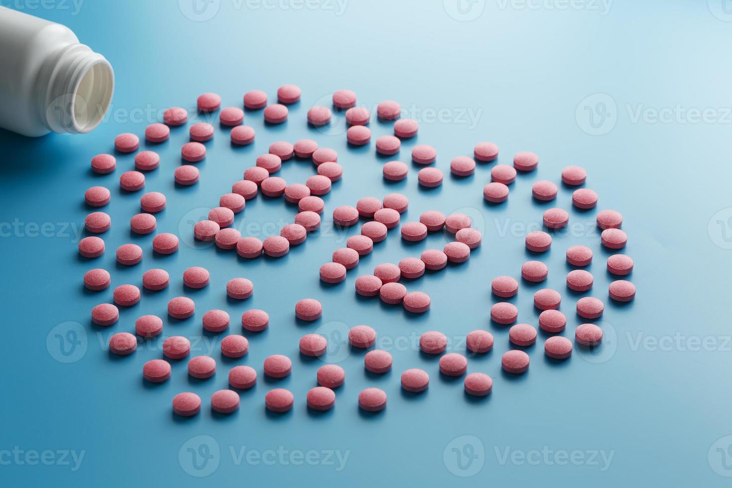 Rosafarbene Tabletten in Form von b12 im Herzen auf blauem Hintergrund, verschüttet aus einer weißen Dose. foto
