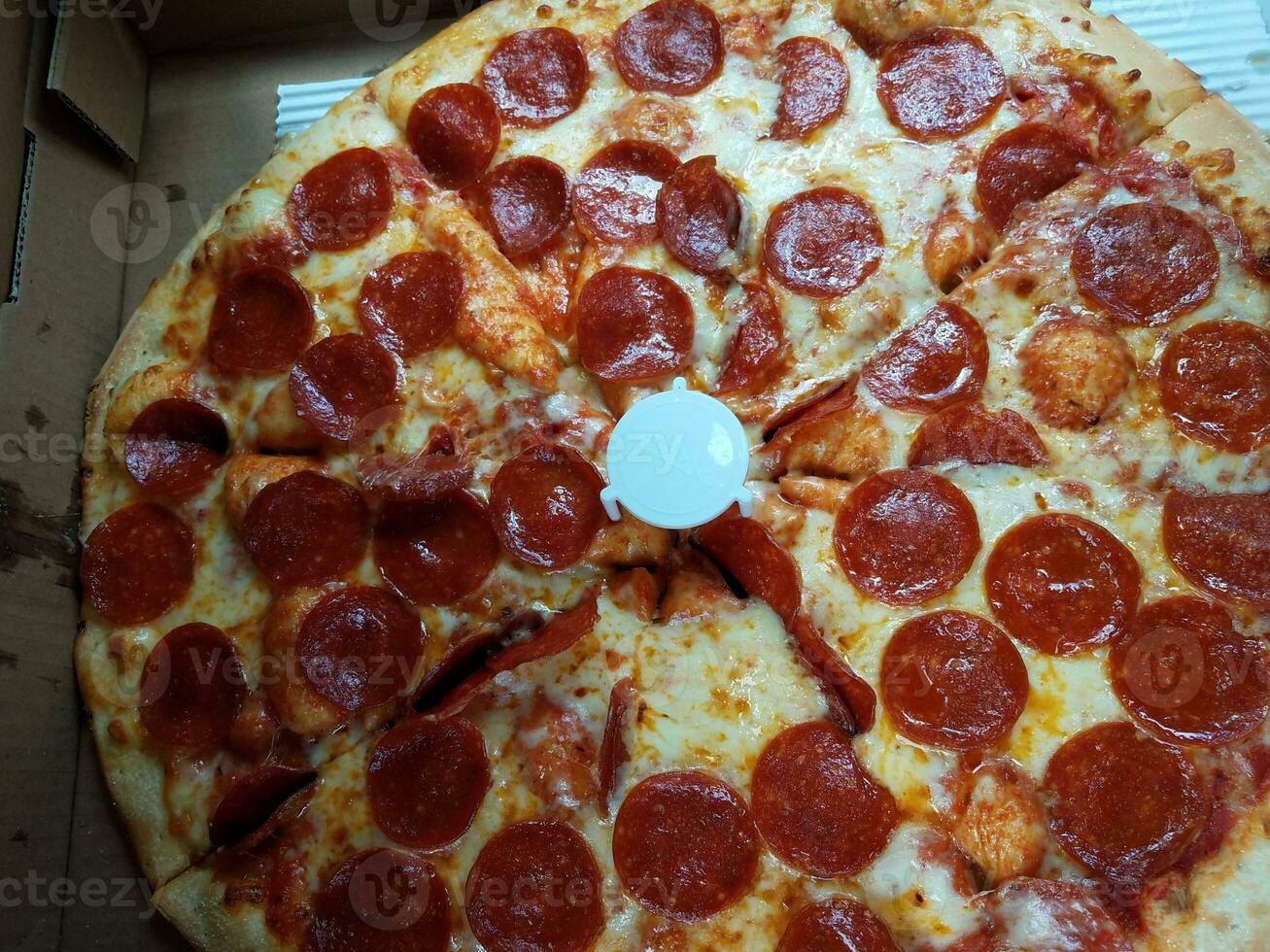 Peperoni-Pizza mit Käse und einem weißen Kunststoffträger foto