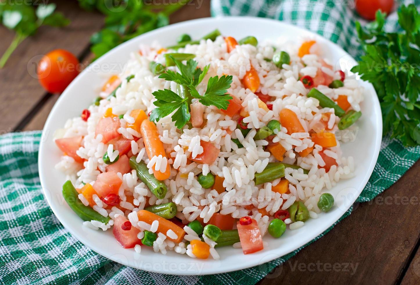 appetitlicher gesunder Reis mit Gemüse in weißer Platte auf einem hölzernen Hintergrund. foto