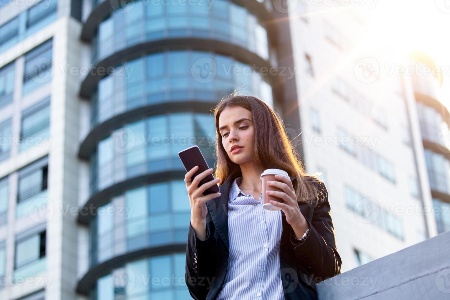 Rechtsanwalt - junge Anwältin, die sich ein mobiles Smartphone ansieht und Kaffee aus einem Einweg-Pappbecher trinkt. junge geschäftsfrau beruflich in der stadt foto