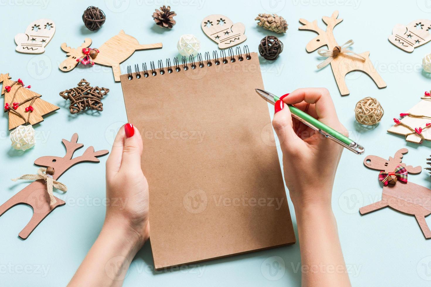 Draufsicht der weiblichen Hand, die einige Notizen in Noteebok auf blauem Hintergrund macht. neujahrsdekorationen und spielzeug. Weihnachtszeit-Konzept foto