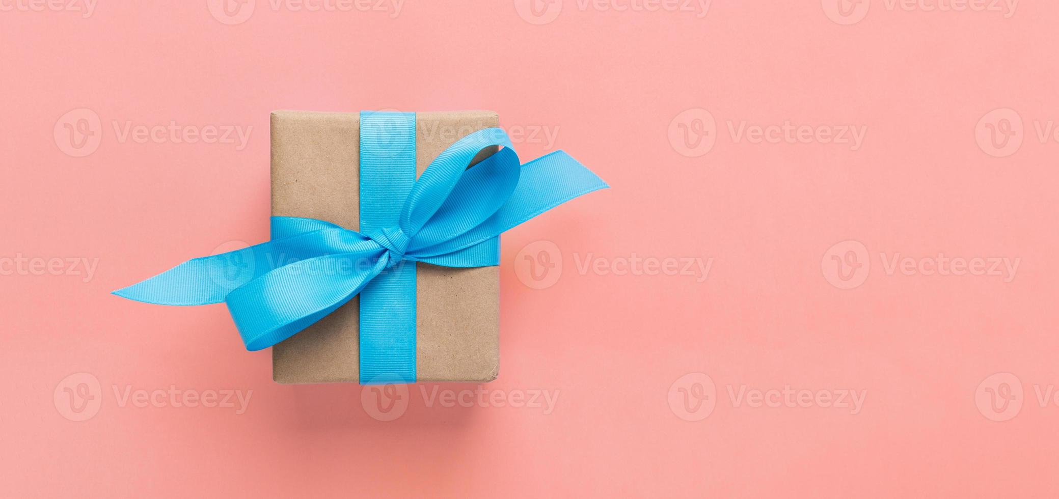 Geschenk verpackt und dekoriert mit blauer Schleife auf rosa Hintergrund mit Kopierraum. flache Lage, Draufsicht foto