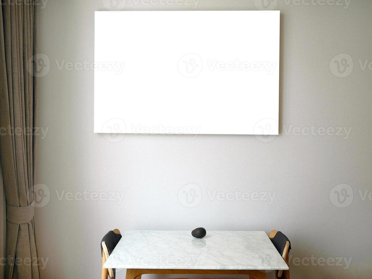 Ein leerer Bilderrahmen auf Leinwand, der an der Wand hängt, hellbrauner Stoffvorhang, Holztisch mit Marmorplatte, zwei Holzstühle, eine Avocadofrucht auf dem Tisch mit Beschneidungspfad foto