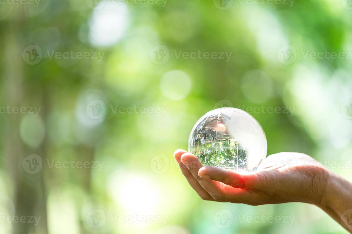 Kristallkugel, die als erzählendes Objekt verwendet wird. Naturpark mit Bäumen im Hintergrund. Hand für Umwelt, Soziales und Governance in nachhaltigem und ethischem Wirtschaften auf grünem Hintergrund. foto