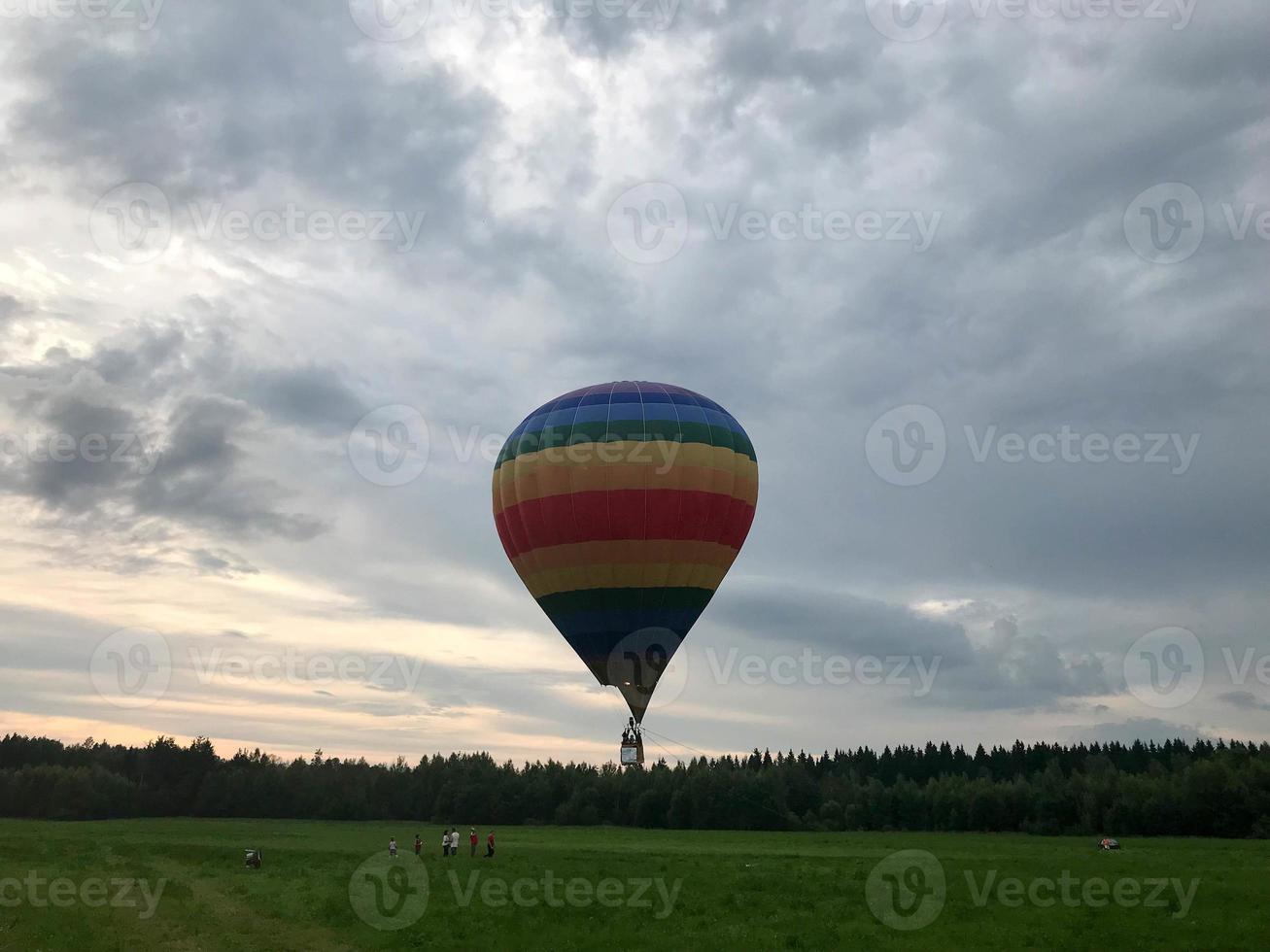 großer, bunter, heller, runder, regenbogenfarbener, gestreifter, fliegender Ballon mit einem Korb gegen den Himmel am Abend foto