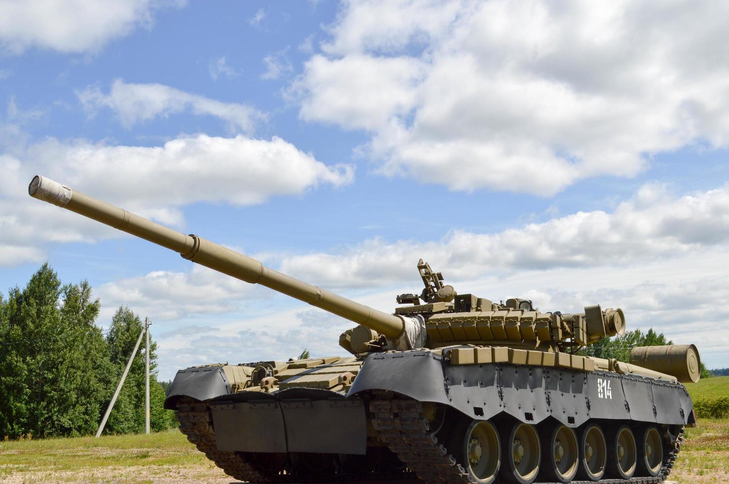 Ein großer, grüner, militärisch gepanzerter, tödlich gefährlicher russischer syrischer Kampfpanzer aus Eisen mit einem Geschützturm und einer Gans ist vor blauem Himmel und Wolken außerhalb der Stadt geparkt foto