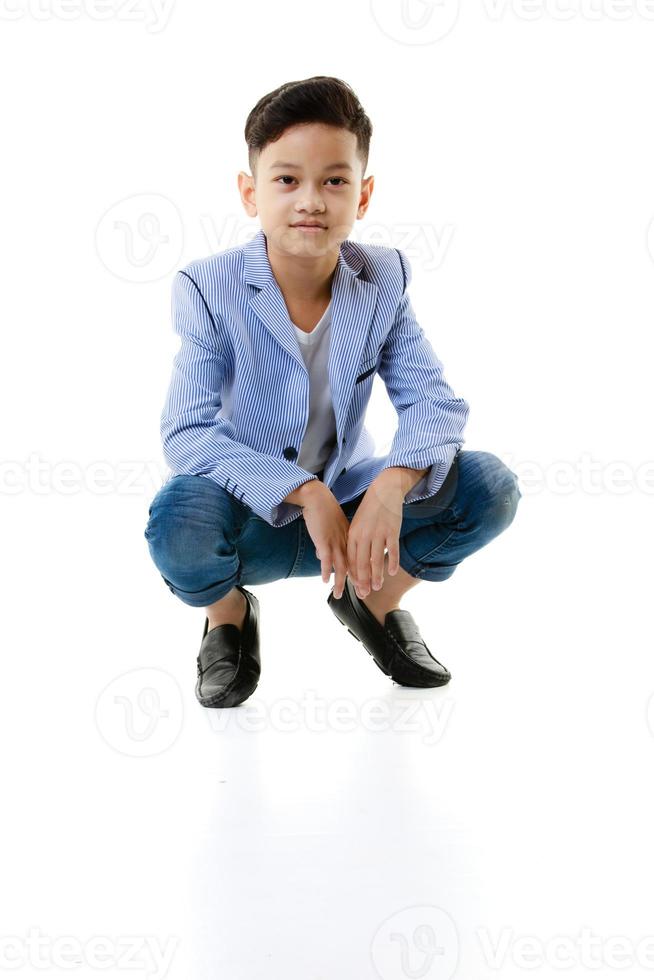 ein 10-jähriger asiatischer junge in einer lässigen jacke sitzt schlau und glücklich und schaut vor einem weißen isolierten hintergrund auf die kamera. foto