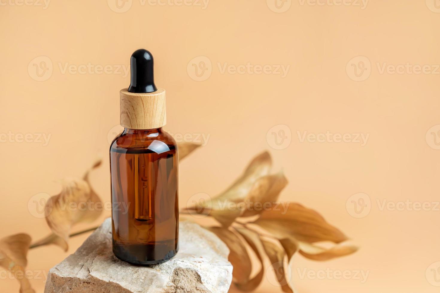 bernsteinfarbene Tropfflasche mit Serum auf Steinpodium. beiger hintergrund mit trockenen blättern. Schönheitskonzept für Gesichts- und Körperpflege. Hautpflegeprodukte, Naturkosmetik. foto