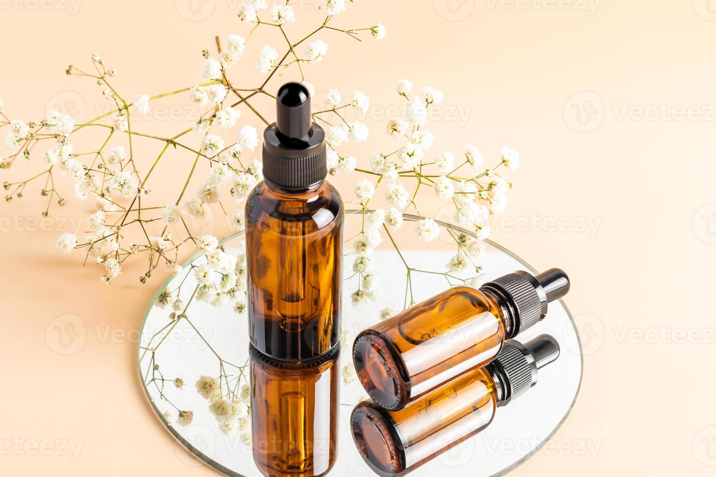 Zwei Glasflaschen mit Tropfer für die Gesichtspflege auf einem runden Spiegel mit weißem Gypsophila. Naturkosmetik. feuchtigkeitsspendend. beiger Hintergrund. foto