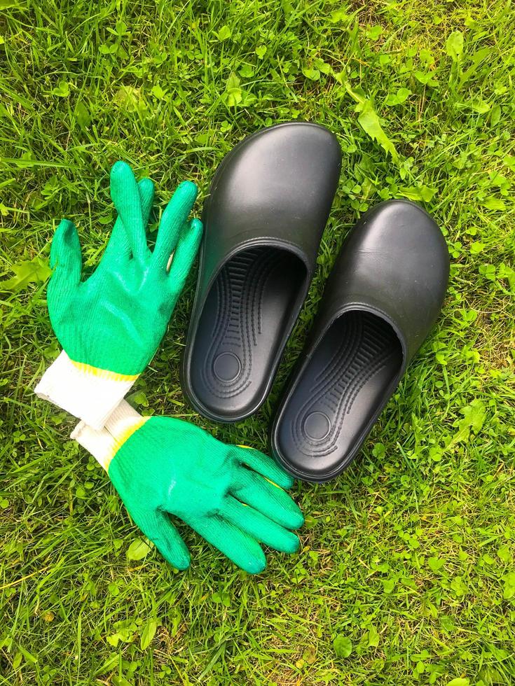 auf dem grünen gras liegen gummigaloschen und grüne bauhandschuhe. Gartengeräte. Gartenbau, Landwirtschaft. Anbau von Pflanzen für die Winterernte und Tiernahrung. Herbsternte foto