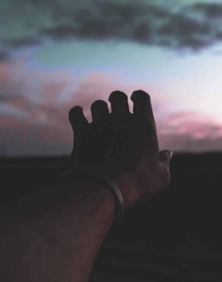 Hand streckt den Sonnenuntergang bei natürlichem schlechten Licht aus foto