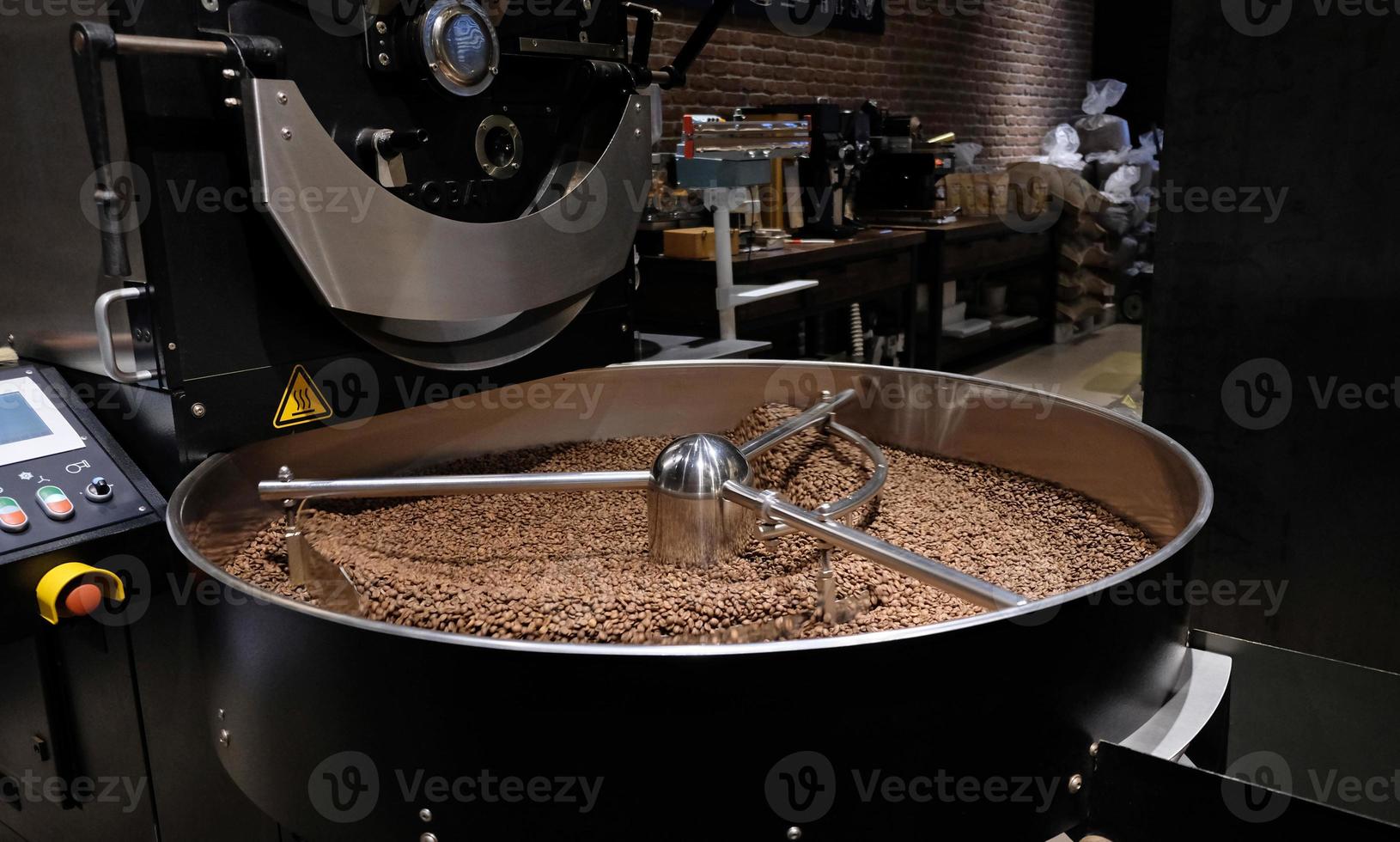 Kaffeeröstmaschine beim Kaffeerösten. Kaffeebohnen mischen. geröstete rotierende Kühler professionelle Maschinen und frische braune Kaffeebohnen Bewegung Nahaufnahme dunkles Foto im Werk.