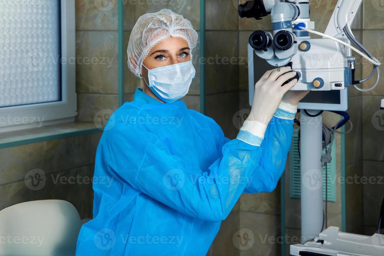 Ärztin in Atemmaske überprüft vor der Arbeit das Operationsmikroskop foto