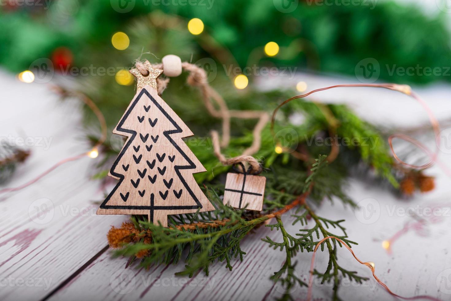 Bastelgeschenk hölzerner Weihnachtsbaumanhänger auf einem Hintergrund von Bokeh-Weihnachtsgirlanden und Weihnachtsbaum. weihnachtsbaumschmuck in form einer weihnachtsbaumnahaufnahme foto