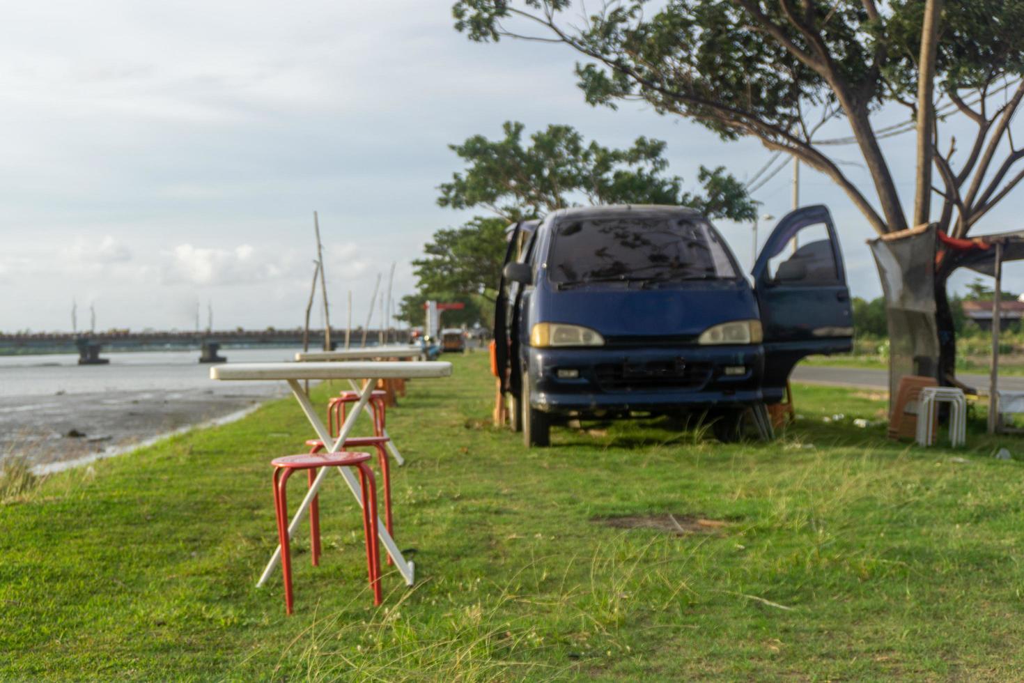 Stuhl und Tisch vor Wohnmobil. Picknick-Konzept. Wohnmobil geparkt unter dem Baum und neben dem Fluss. konzept des mobilen cafés foto