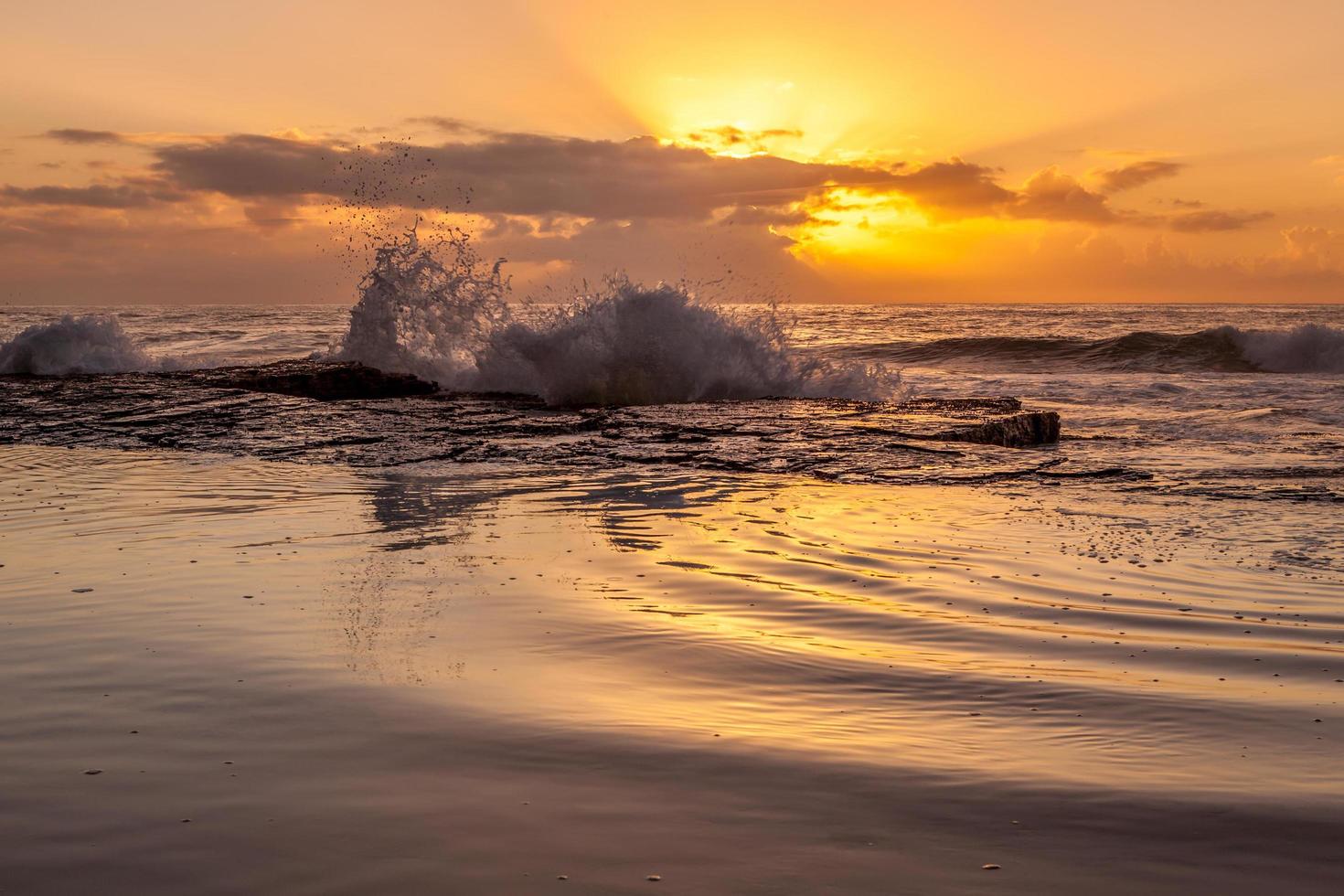 Ozeanwellen, die während des Sonnenuntergangs am Ufer abstürzen foto