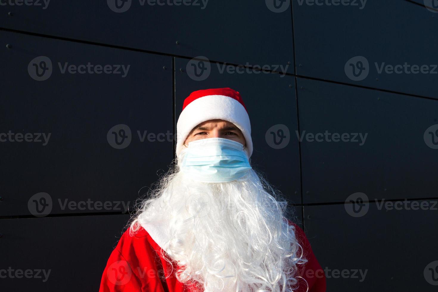 weihnachtsmann mit weißem bart im roten mantel in einer medizinischen maske. weihnachten in der coronavirus-pandemie, saisonale krankheiten, sars und lungenentzündung in den ferien. Schutz vor Viren im neuen Jahr foto