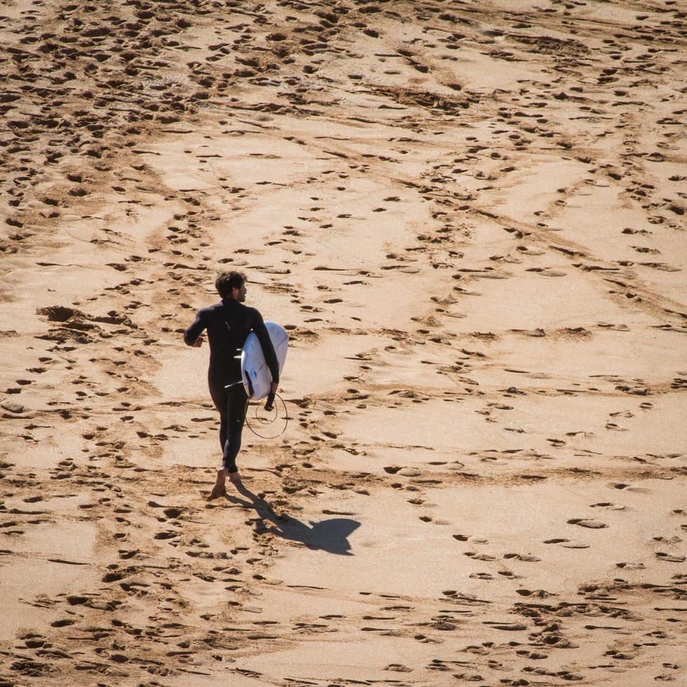 Sydney, Australien, 2020 - Mann, der mit einem Surfbrett auf einem Strand geht foto