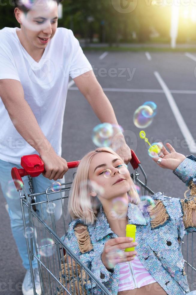 paar haben spaß mit einem einkaufswagen und blasen auf einem supermarktparkplatz foto