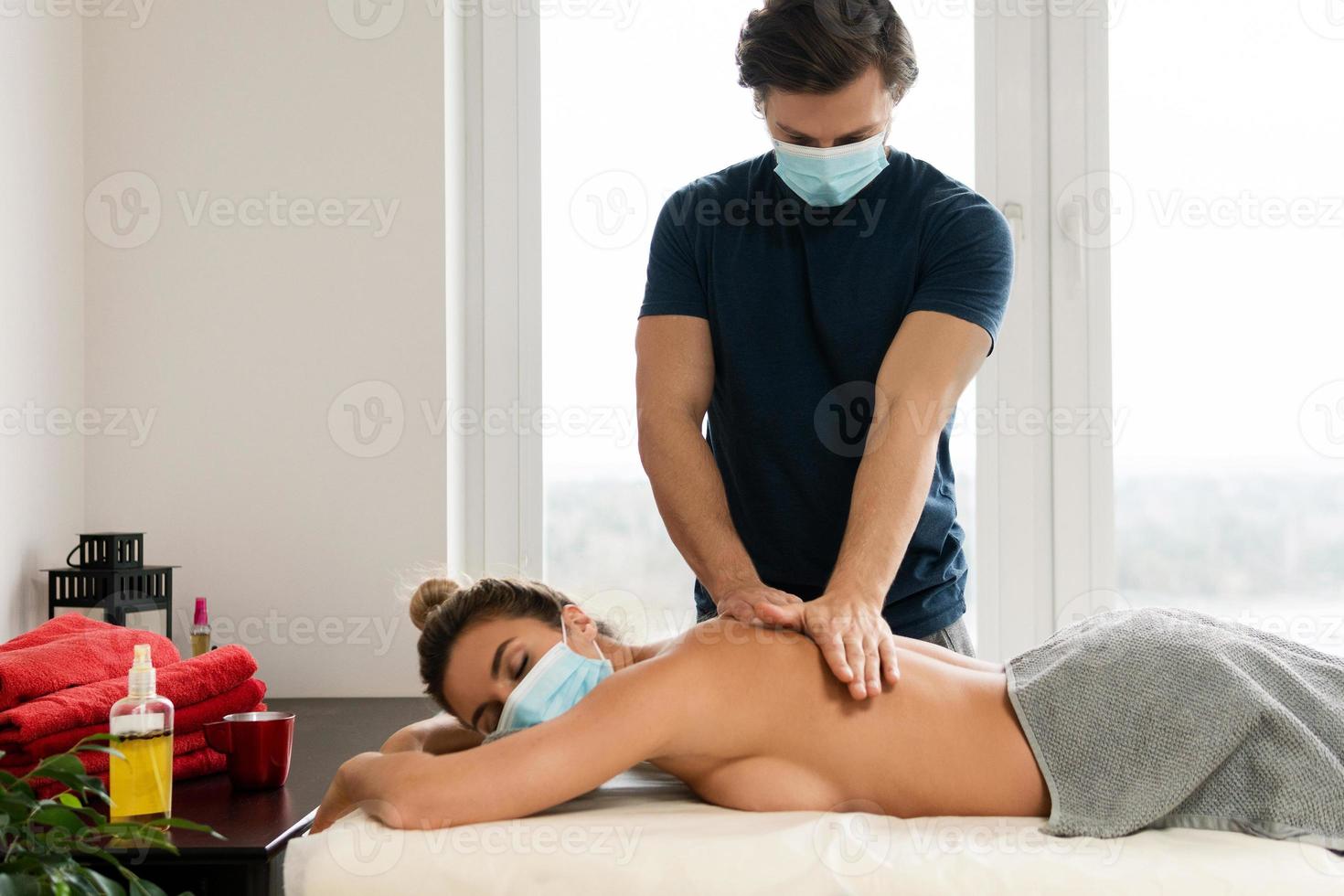 masseur mann mit präventionsmaske, der rückenmassage für seine klientin macht foto