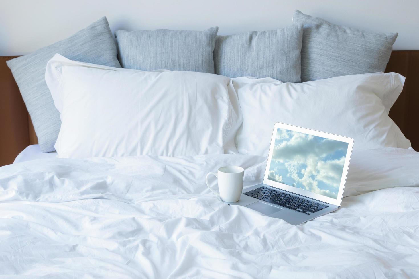 Laptop-PC und eine Tasse Kaffee auf dem Bett foto