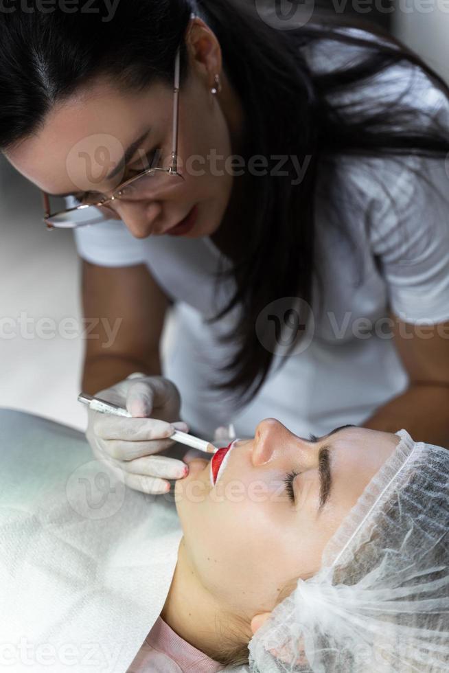 Permanent Make-up-Künstlerin und ihre Kundin während des Lippenröten-Verfahrens foto