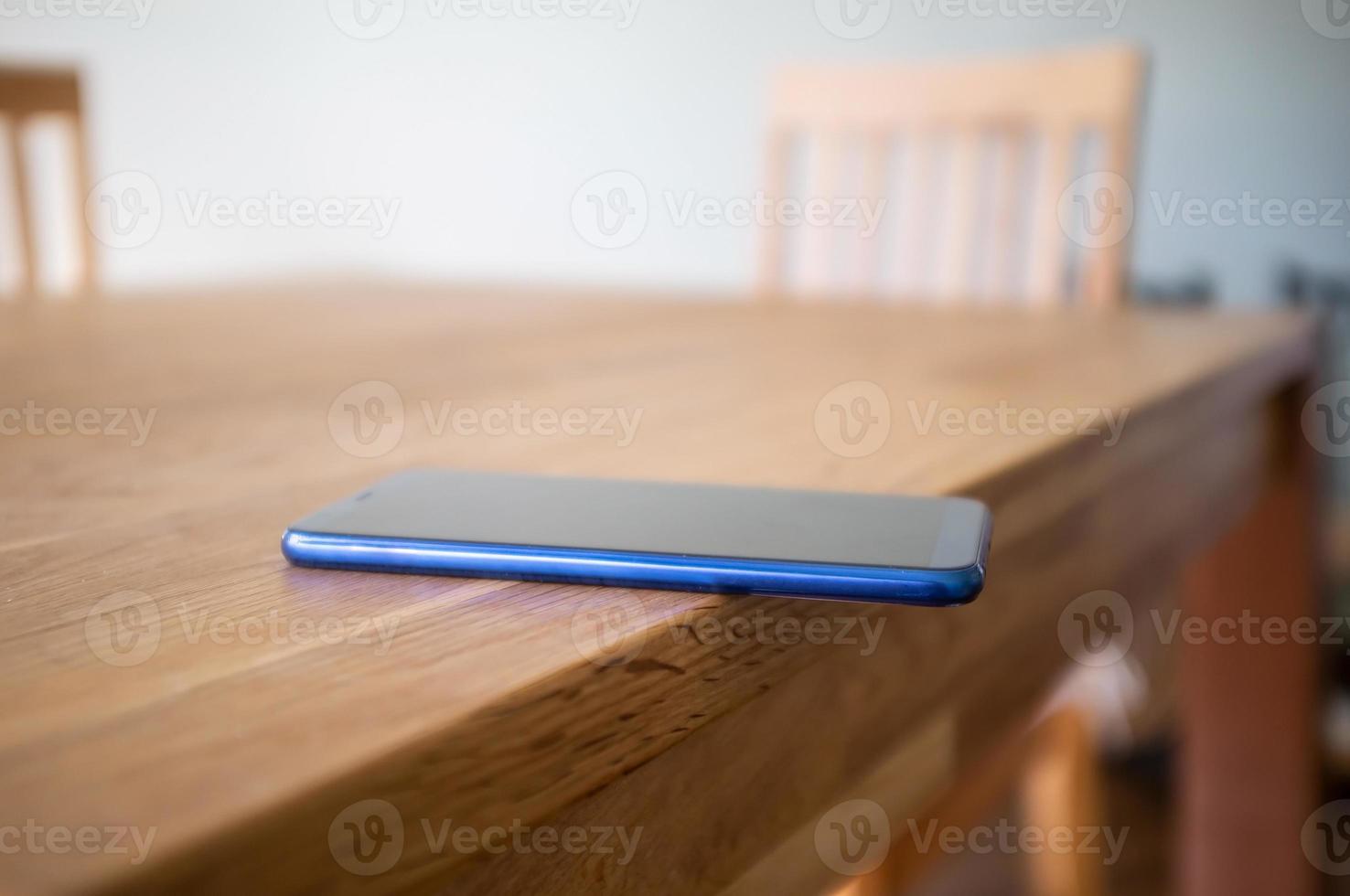 Smartphone wird achtlos auf die Kante eines Holztisches gelegt und kann herunterfallen. konzept der nachlässigen einstellung zu dingen. foto