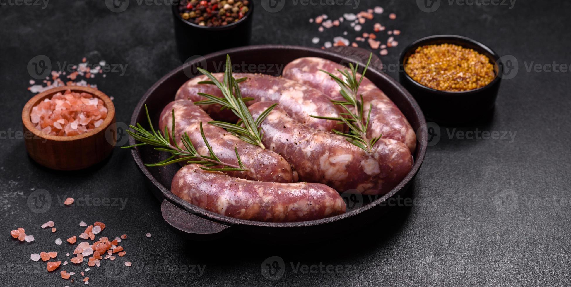 Rohe Schweinswürste grillen mit Gewürzen und Kräutern auf einem dunklen Betontisch foto