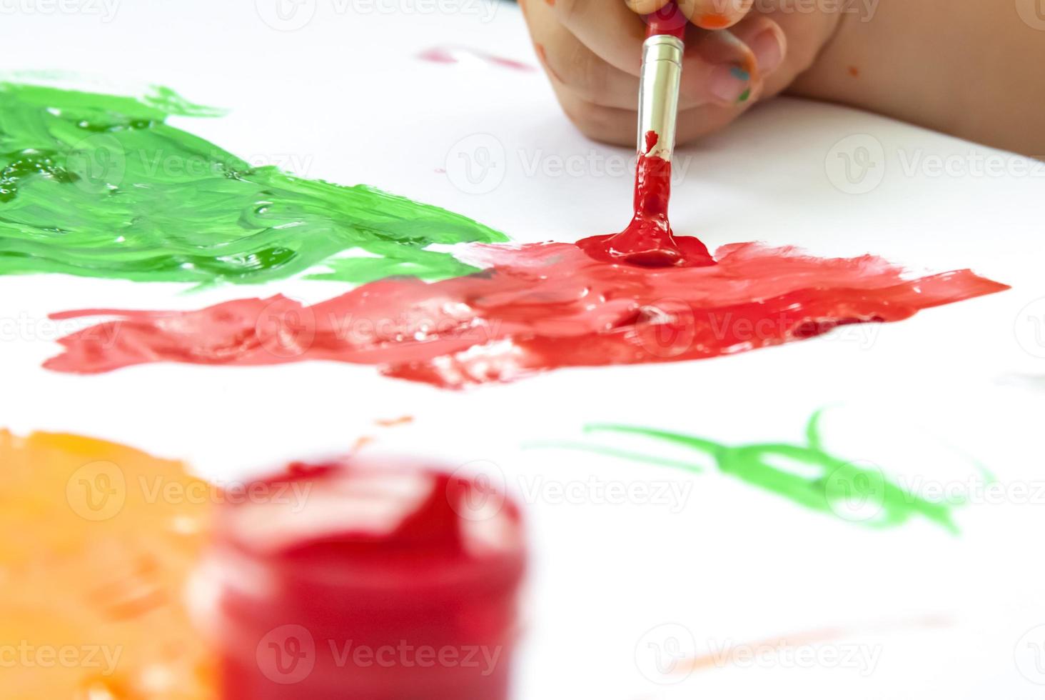 Eine Kinderhand hält einen Pinsel und malt Papier mit großen Strichen. Abstriche heller Farbe auf weißem Papier. foto