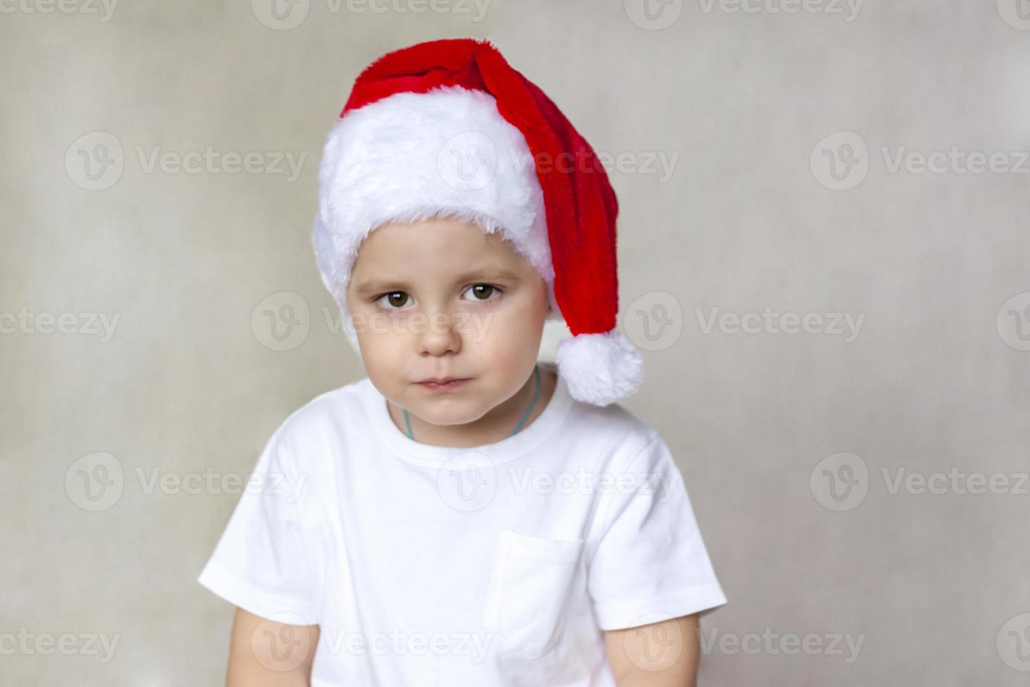 Porträt eines süßen kleinen Jungen in einem weißen T-Shirt und einem Weihnachtsmann-Hut. die Emotionen der Kinder. weihnachten und neujahr. erfolg, gute idee, kreative ideen und konzepte. foto