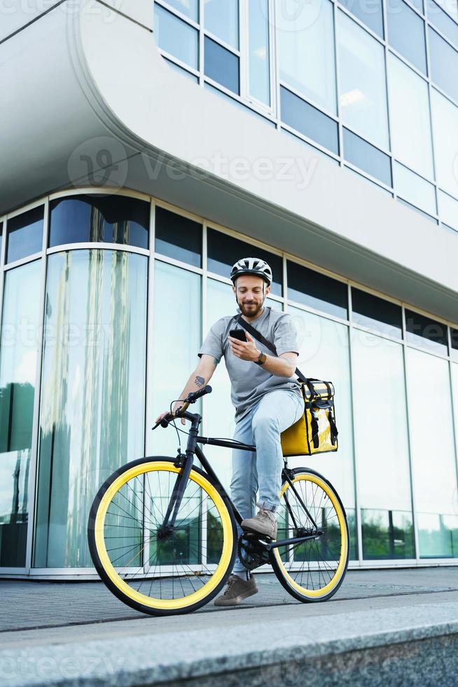 express-kurier mit isolierter tasche, die das telefon auf dem fahrrad betrachtet. foto