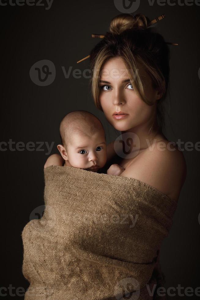 Schöne Mutter und ihr kleines Baby sind in Sackleinen gehüllt foto