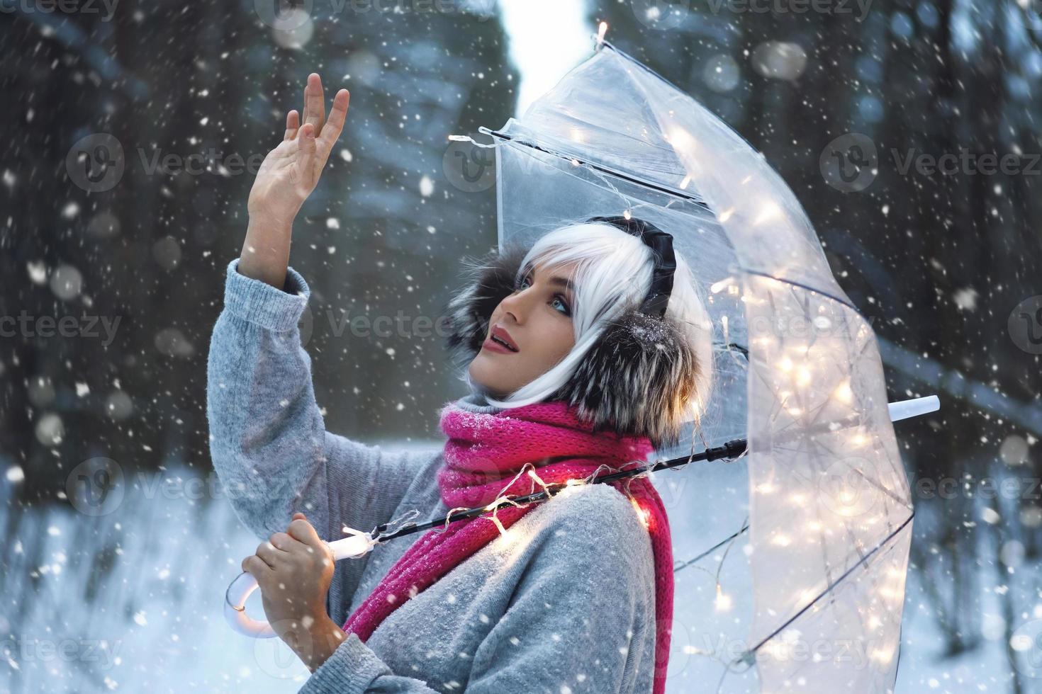 junge frau, die an einem verschneiten wintertag unter einem transparenten regenschirm spazieren geht foto
