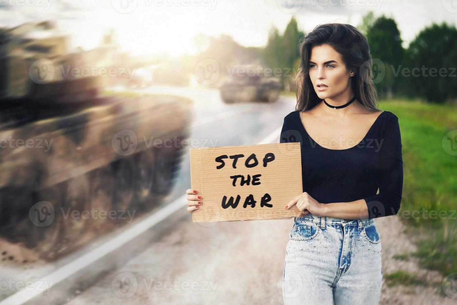 Aktivistin mit Banner stoppt den Krieg in der Nähe der Straße mit fahrenden Panzern foto