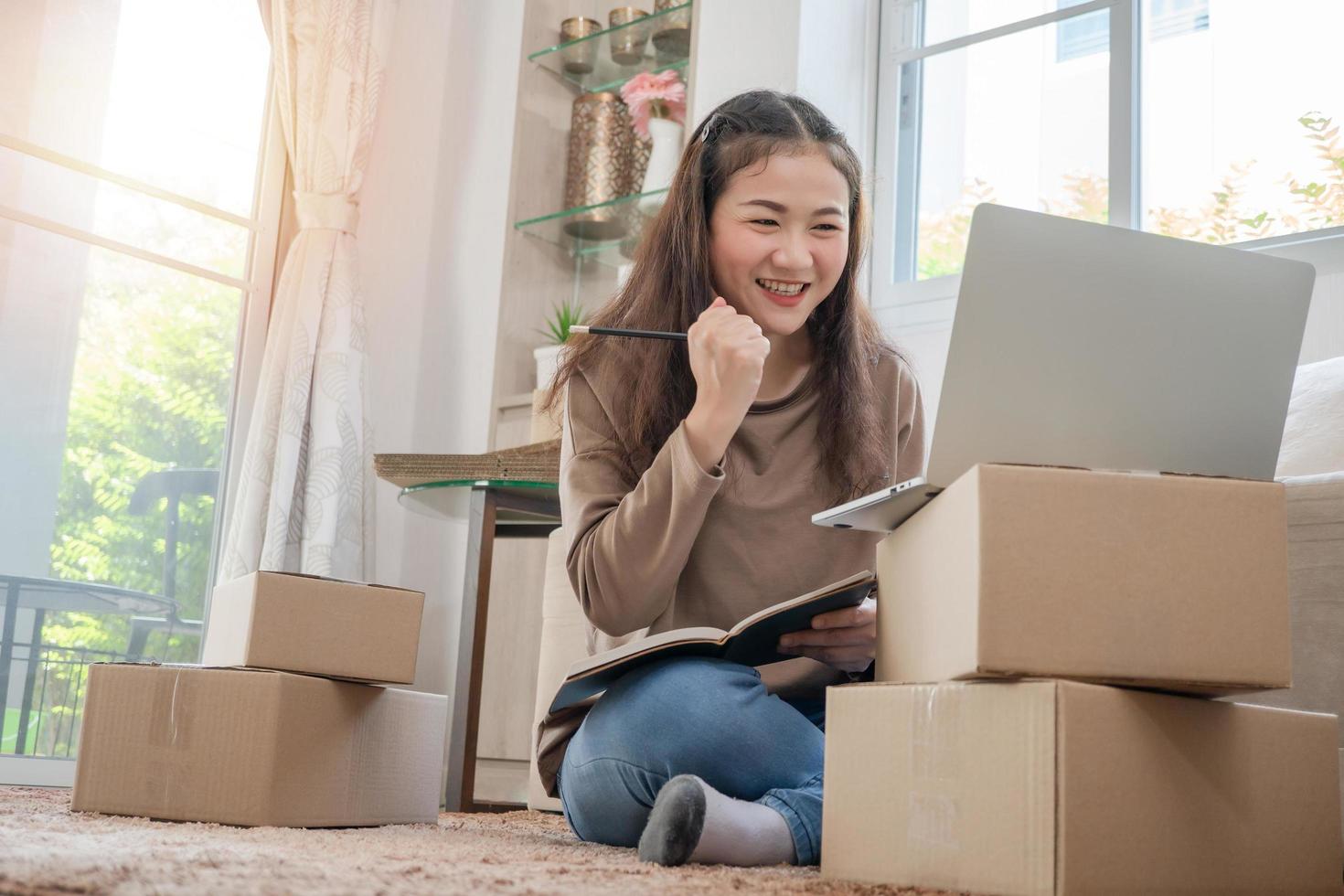 Fröhlicher asiatischer Jungunternehmer, Lächeln für den Verkaufserfolg, nachdem die Bestellung im Online-Shopping-Shop im Laptop zu Hause überprüft wurde, Konzept des Online-Händlergeschäfts und E-Commerce foto