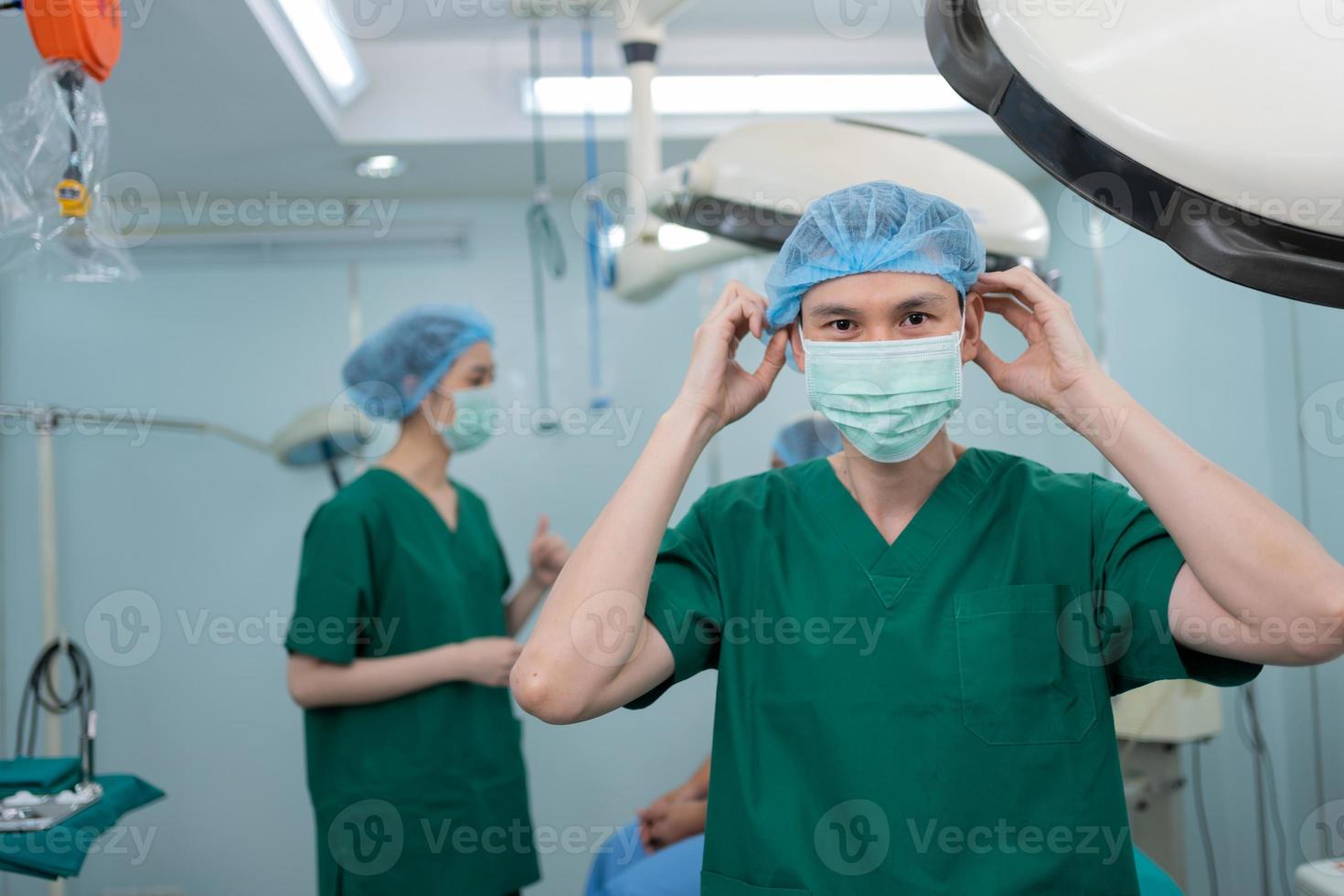 Porträt eines asiatischen Chirurgen mit medizinischer Maske, der im Operationssaal eines Krankenhauses steht. Team von professionellen Chirurgen. gesundheitswesen, rettungsdienstkonzept foto