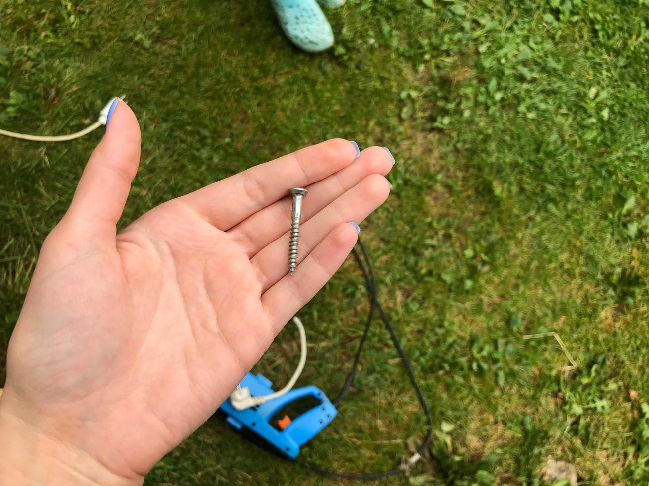 das mädchen mit blauer maniküre hat einen langen nagel in ihrer handfläche. Metallnagel, Silber, Chrom. vor dem hintergrund von gras und werkzeugen zur reparatur. hausbau selber machen foto