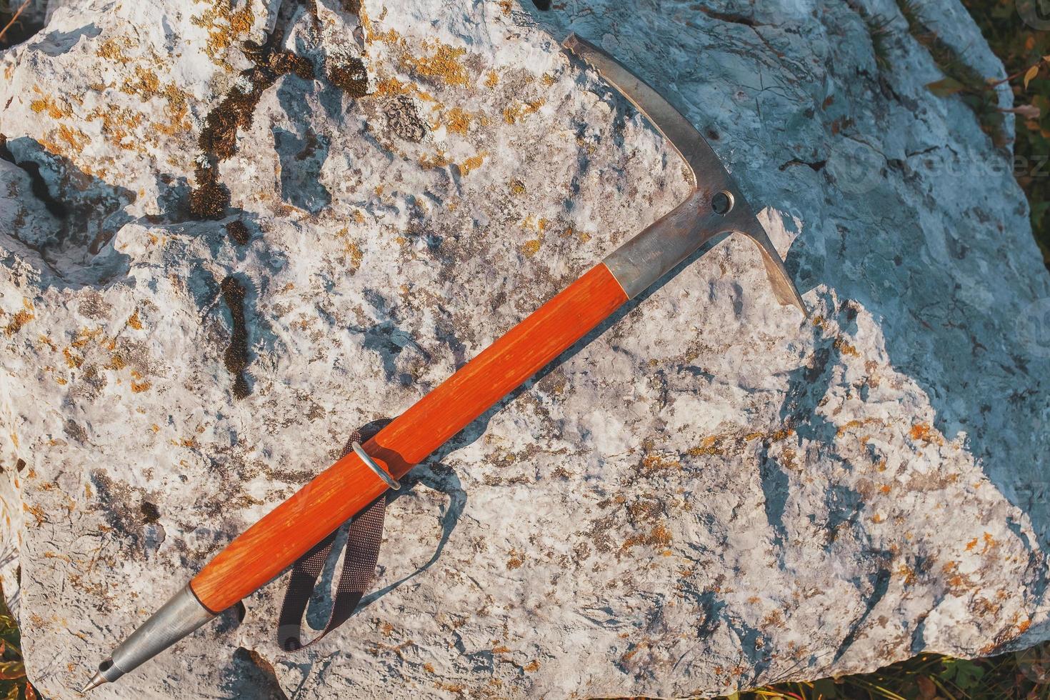 Ein Eispickel mit orangefarbenem Holzgriff liegt auf einem grauen Stein. reisen foto