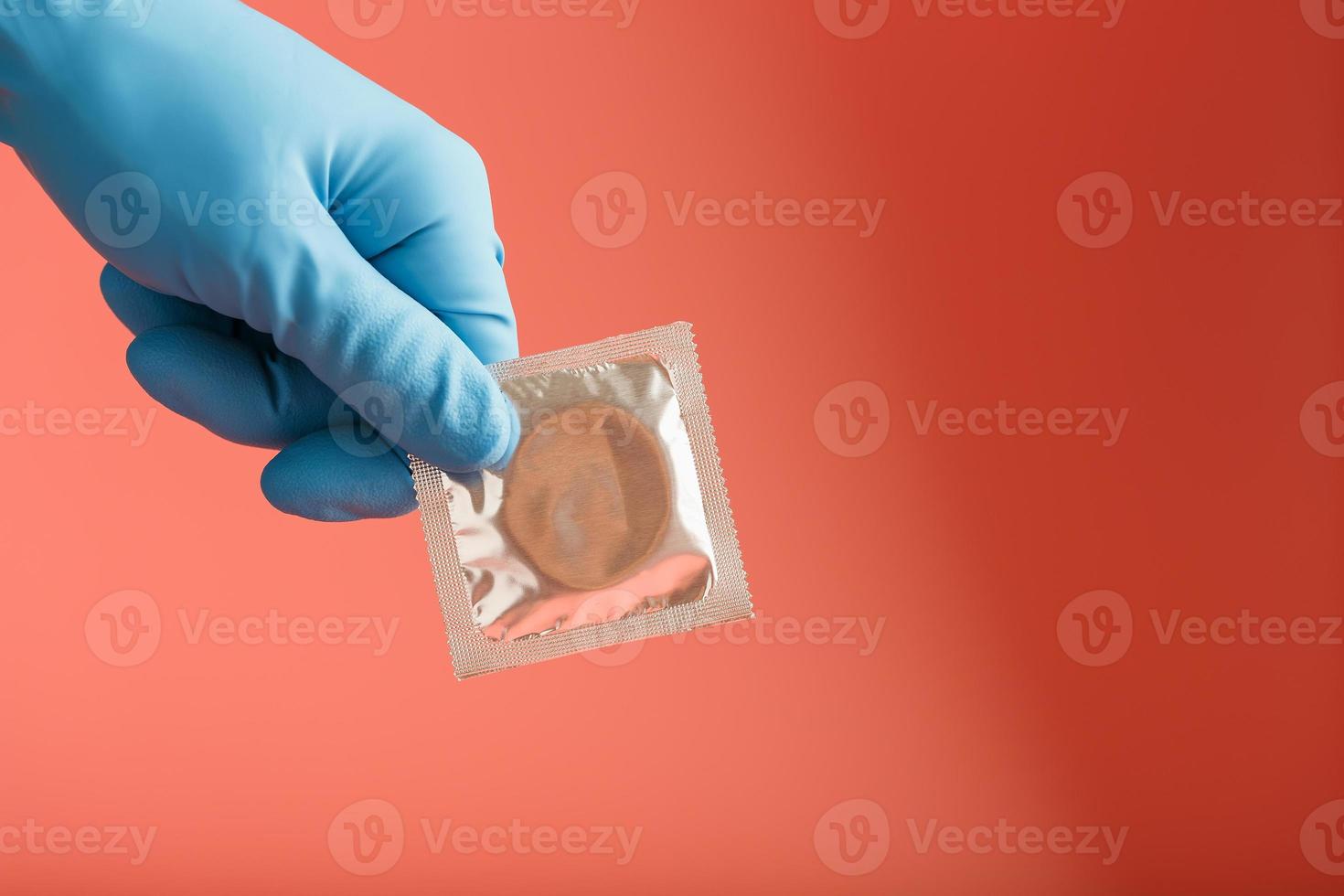 die hand des arztes in einem blauen handschuh hält ein kondom in einer packung auf rosa hintergrund. Spermalatex und Schutz vor Schwangerschaft. foto