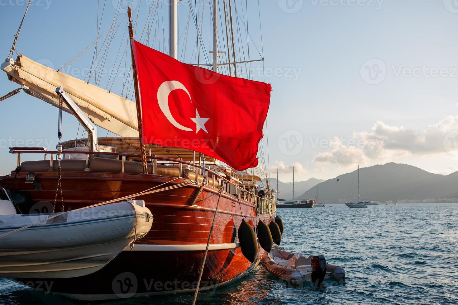 Schöne Holzyacht mit der großen Flagge der Türkei auf dem Pier, vor dem Hintergrund eines wunderschönen Sonnenuntergangshimmels mit Sonnenstrahlen foto