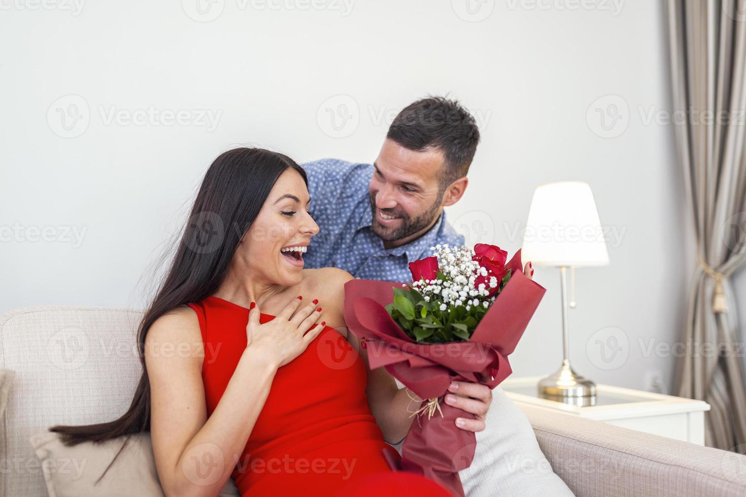 aufgeregte junge frau, die unerwarteten strauß roter rosen vom ehemann zu hause erhält, liebevoller großzügiger freund, der attraktive freundin am valentinstag romantisch überrascht foto