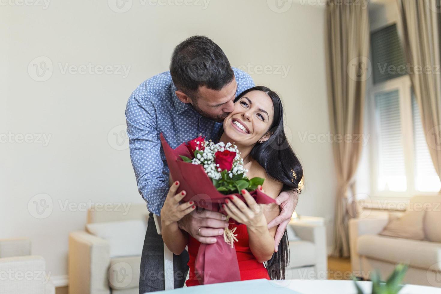 liebevoller junger mann, der seiner schönen jungen frau einen strauß roter rosen schenkt und sie am valentinstag küsst, romantische glückliche paare, die am valentinstag geschenke teilen foto