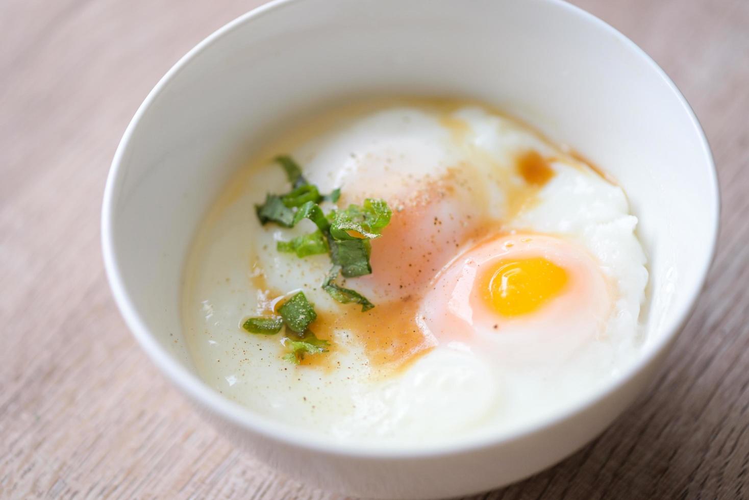 eifrühstück, weich gekochte eier auf weißer schüssel mit pfeffer, koriander auf holztisch, onsen tamago ei - ei mikrowelle foto
