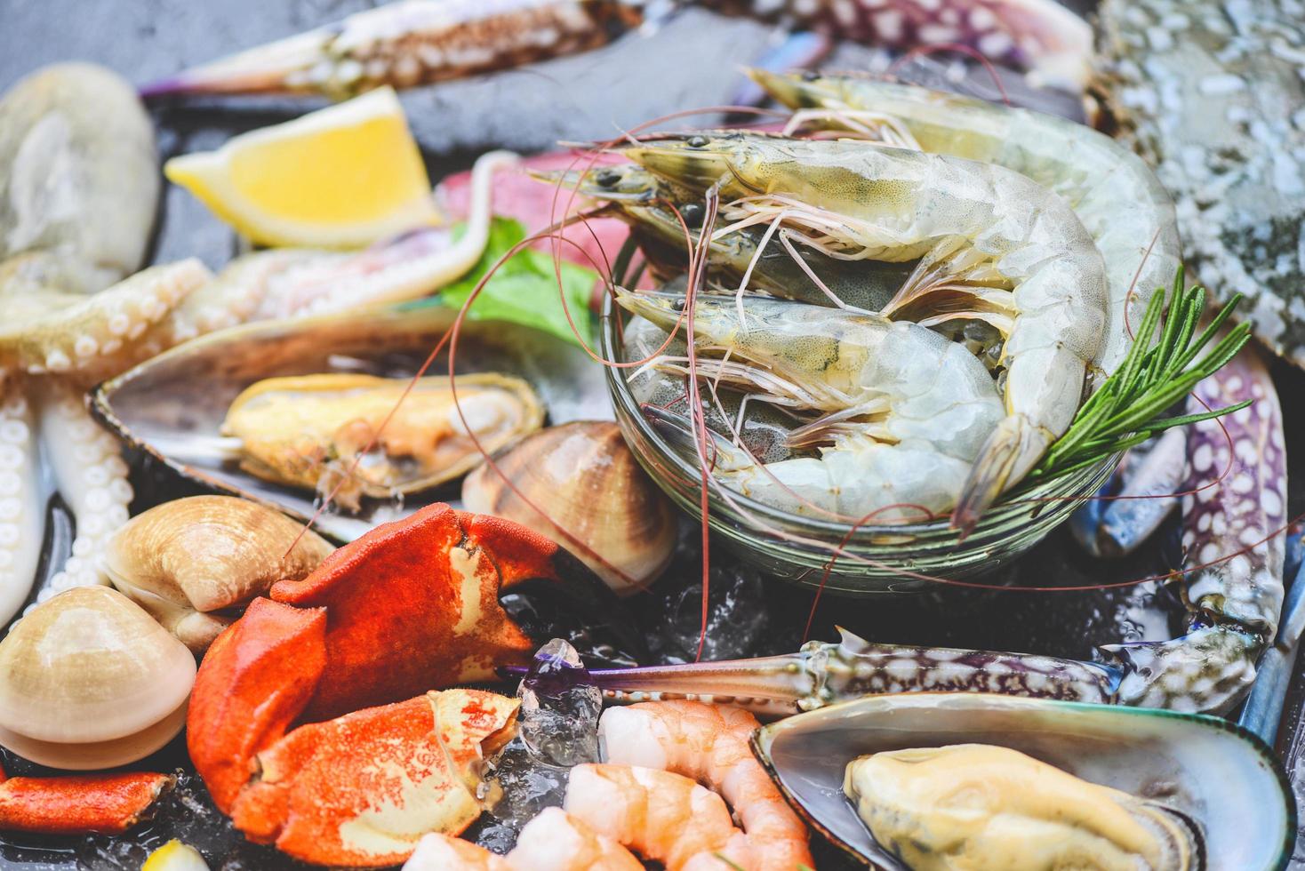 Meeresfrüchte Schalentiere auf Eis gefroren mit Garnelen Garnelen Krabbenscheren Muscheln Tintenfische Tintenfische und Muscheln im Restaurant frisches rohes Meeresfrüchtebuffet mit Zitrone Rosmarin Zutaten Kräuter und Gewürze foto