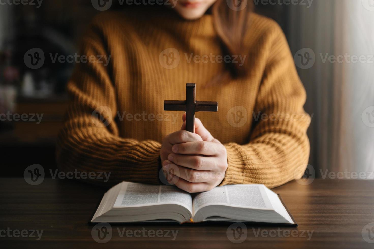 frau, die sitzt und die schriften studiert. das holzkreuz in den händen. christliche bildungskonzepte die heilige schrift öffnen und beten foto