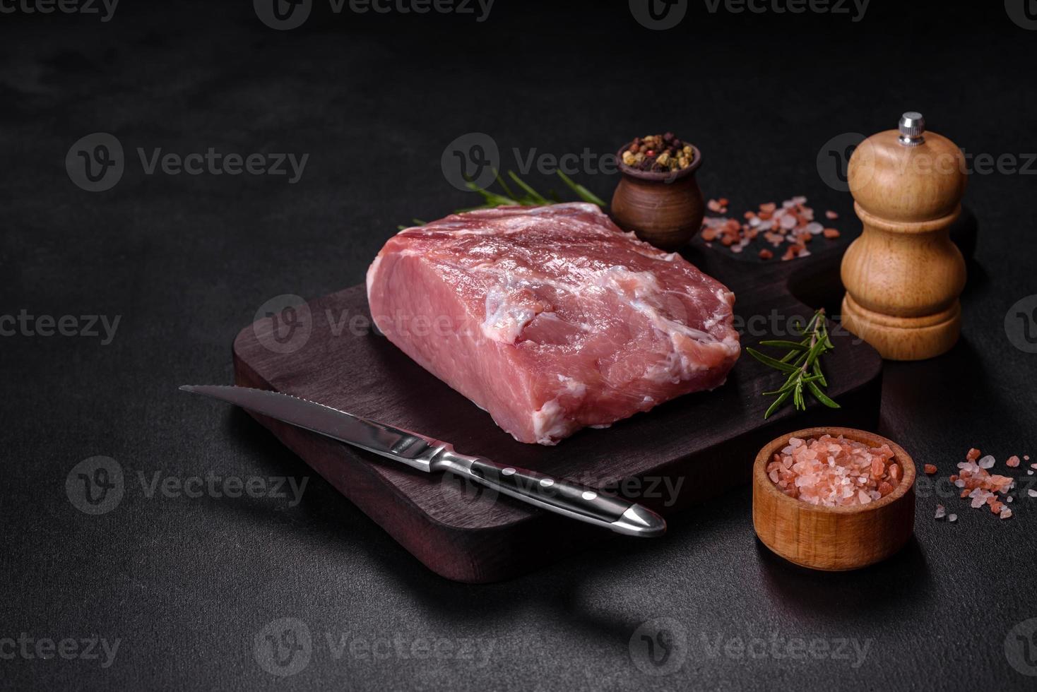 frisches Stück rohes Schweinefleisch mit Gewürzen, Salz und Kräutern auf einem Holzschneidebrett foto